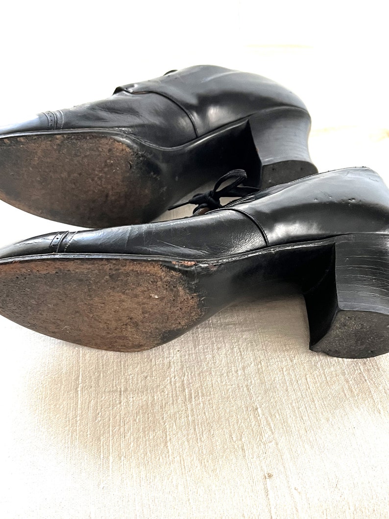 May include: A pair of black leather heeled shoes with lace-up closures. The shoes have a rounded toe and a block heel.