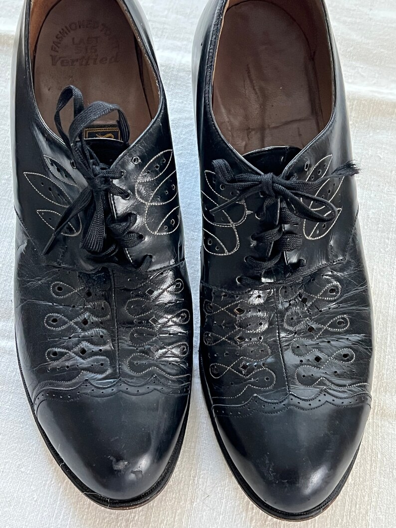 May include: A pair of black leather lace-up shoes with decorative stitching and a white label on the inside that reads "Fashioned for Ladies Verified".