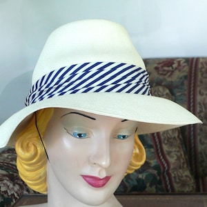 May include: A white wide-brimmed hat with a blue and white striped band. The hat is on a mannequin head with blonde hair.