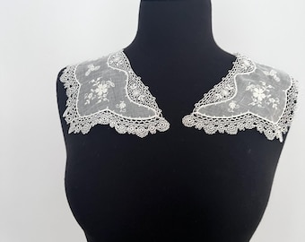 May include: A pair of white lace collars with floral embroidery, displayed on a black mannequin. The collars feature a delicate scalloped edge and intricate detailing. The design is elegant and the lace is fine.