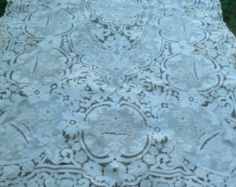 May include: White lace tablecloth with a delicate floral pattern. The tablecloth has a central oval design with intricate details.
