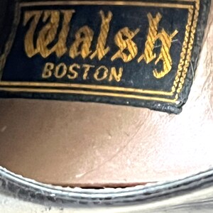 May include: Close-up of a black leather shoe with a gold embossed label that reads "Walsh Boston".