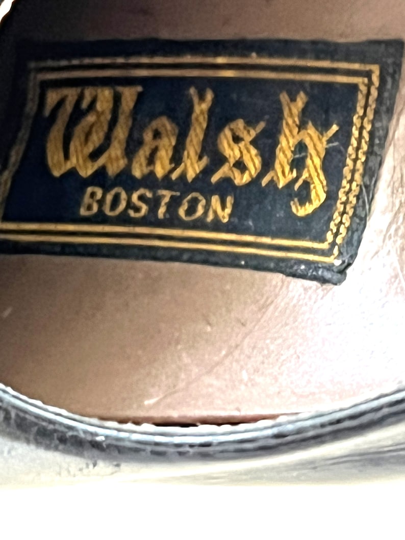 May include: Close-up of a black leather shoe with a gold embossed label that reads "Walsh Boston".