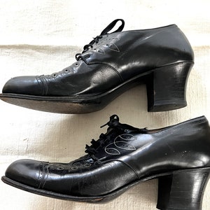 May include: A pair of black leather heeled shoes with lace-up closures and decorative stitching. The shoes have a rounded toe and a block heel.