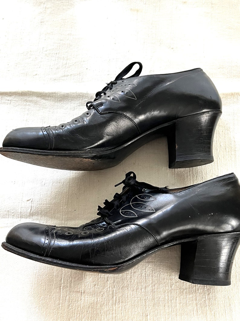 May include: A pair of black leather heeled shoes with lace-up closures and decorative stitching. The shoes have a rounded toe and a block heel.