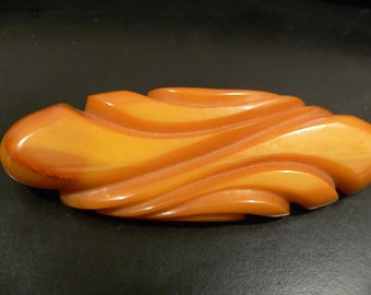 May include: A large, abstract, amber-colored, plastic brooch with a wavy, flowing design.