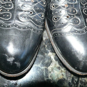May include: A pair of black leather shoes with a decorative pattern of holes and stitching. The shoes have a pointed toe and a lace-up closure.