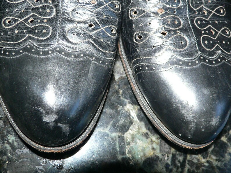 May include: A pair of black leather shoes with a decorative pattern of holes and stitching. The shoes have a pointed toe and a lace-up closure.