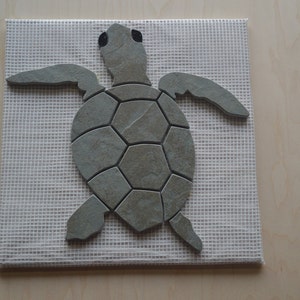 May include: A gray stone mosaic turtle on a white mesh background. The turtle is made of small, irregular shaped stones.