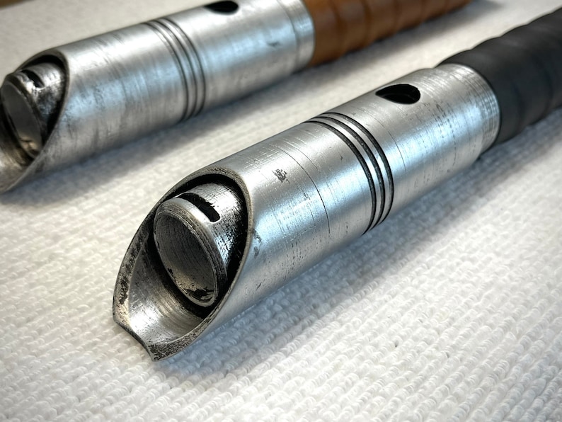 K&ouml;nnte beinhalten: Nahaufnahme der silbernen Metallspitze eines Lichtschwertgriffs. Der Griff hat eine strukturierte Oberfl&auml;che und einen schwarzen Gummibeschlag.