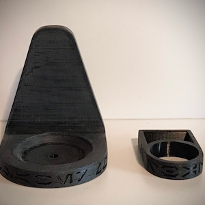 May include: Two 3D printed black plastic wall mounts. The larger mount has a circular base with the text "SM-7-D" printed on it. The smaller mount is a ring with the text "HEX" printed on it.