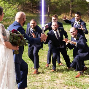 K&ouml;nnte beinhalten: Eine Hochzeitsgesellschaft posiert f&uuml;r ein Foto, wobei der Br&auml;utigam ein blaues Lichtschwert h&auml;lt. Das Brautpaar steht im Vordergrund, w&auml;hrend die Trauzeugen im Hintergrund sind. Die Trauzeugen tragen alle dunkle Anz&uuml;ge und machen spielerische Posen.