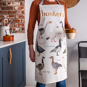 May include: A white apron featuring a colourful illustration of various types of geese. The apron has the text "honkers" in gold lettering at the top. The geese are labelled with their names, including "Emperor", "Barnacle", "Bean", "Snow", and "Cackling".