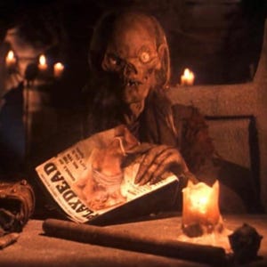 Puede incluir: Una figura esquelética con un solo ojo se sienta en una habitación tenuemente iluminada, leyendo una revista titulada "Playdead" con una vela encendida a su lado.