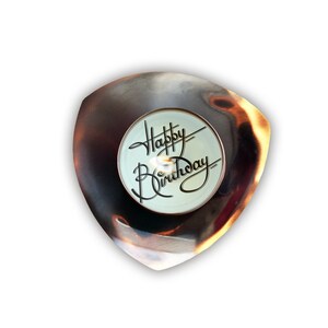 May include: A small, triangular, metal dish with a burnished copper finish. The dish has a white, round, center piece with the words "Happy Birthday" written in black script.