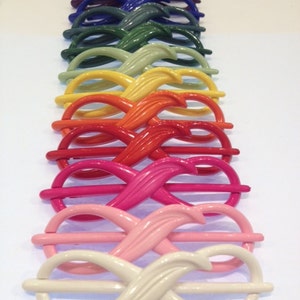May include: A collection of ten hair slides arranged in a row, each featuring a glossy, figure-eight infinity shape with a central pin. The colors range from black, purple, and blue to green, yellow, orange, red, magenta, pink, and off-white.
