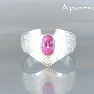 Puede incluir: Un anillo de plata con una piedra ovalada rosa engastada en una banda en forma de V. La banda tiene un acabado texturizado.