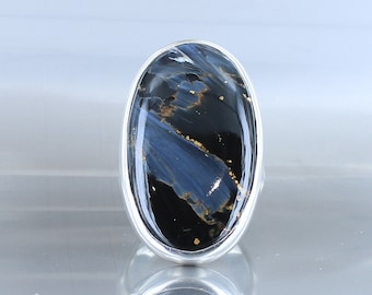 Peut inclure: Une bague en argent avec une grande pierre ovale bleue et noire avec des reflets dorés. La pierre a un motif tourbillonnant.