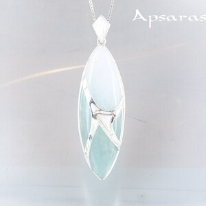 Puede incluir: Un collar con un colgante de plata con una piedra preciosa azul claro y blanca. La piedra preciosa está engastada en un marco de plata con un diseño delicado.