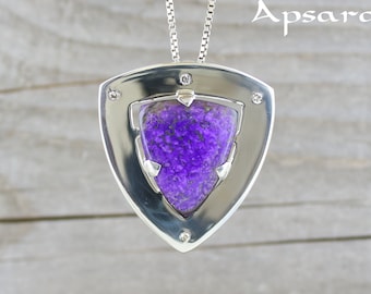 May include: A silver pendant with a purple gemstone set in a triangular frame. The pendant is on a silver chain.