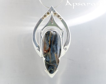 Peut inclure: Un pendentif en argent avec une pierre en œil de tigre bleu et brun sertie dans un motif géométrique. Le pendentif est sur une chaîne en argent.