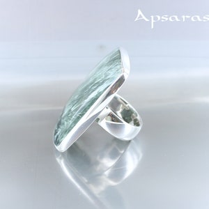 May include: A silver ring with a large, square, green gemstone. The gemstone has a swirling, marbled pattern.
