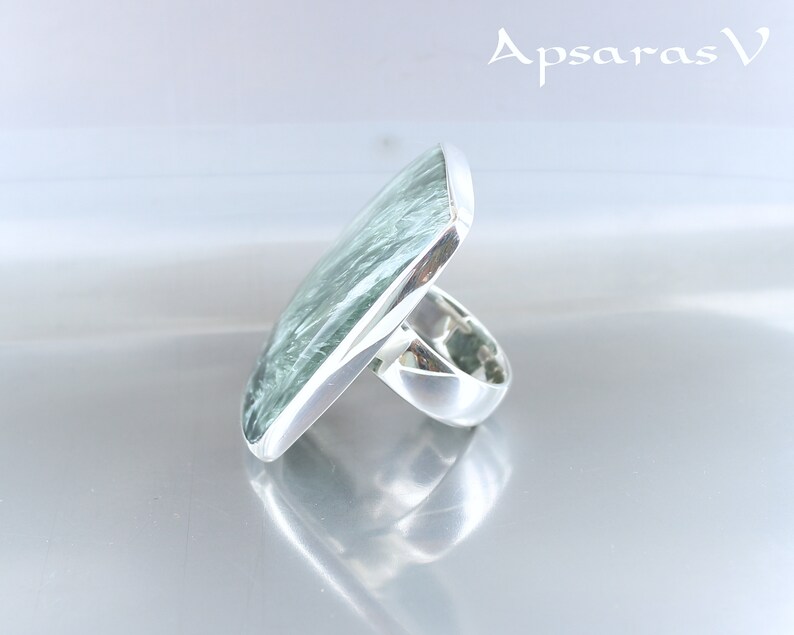 May include: A silver ring with a large, square, green gemstone. The gemstone has a swirling, marbled pattern.