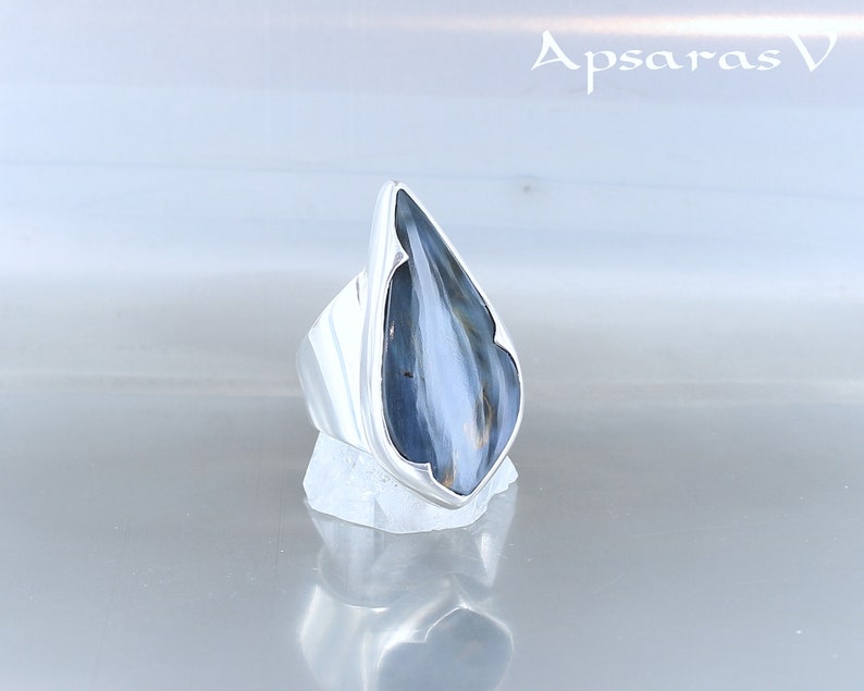 Peut inclure: Une bague en argent avec une pierre pr&eacute;cieuse bleu et blanc en forme de larme. La bague est pos&eacute;e sur un fond blanc.