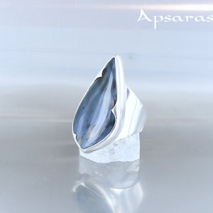 Peut inclure: Une bague en argent avec une pierre pr&eacute;cieuse bleu et blanc en forme de larme. La bague est pos&eacute;e sur un support blanc.