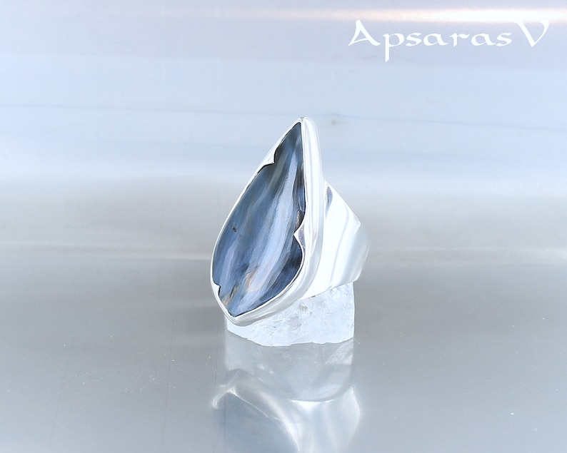 Peut inclure: Une bague en argent avec une pierre pr&eacute;cieuse bleu et blanc en forme de larme. La bague est pos&eacute;e sur un support blanc.