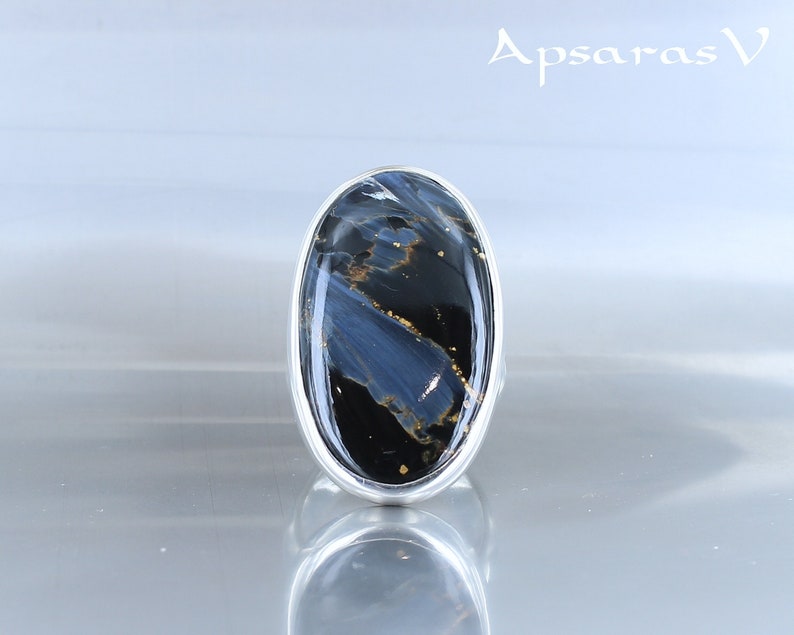 Puede incluir: Un anillo de plata con una gran piedra ovalada azul y negra con motas doradas. La piedra tiene un patr&oacute;n de remolino.