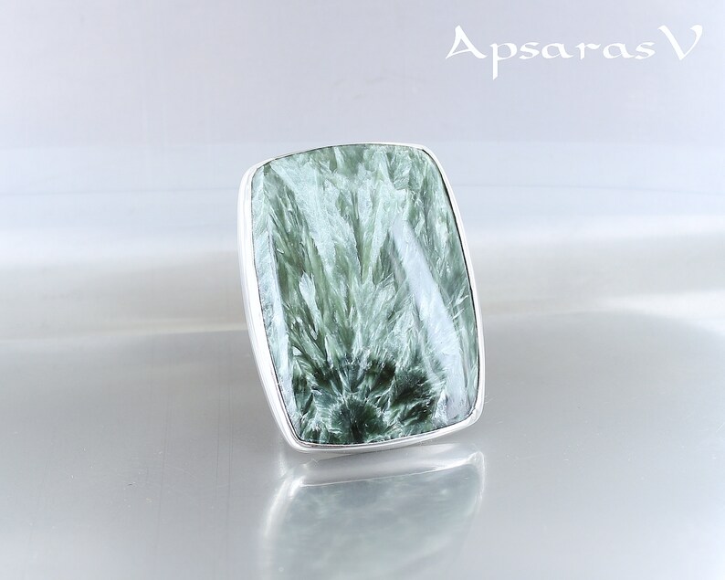 May include: A silver ring with a large, rectangular green gemstone. The gemstone has a swirling, marbled pattern.