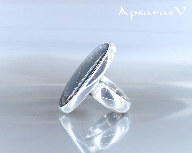 Puede incluir: Un anillo de plata con una piedra ovalada negra engastada en el centro. El anillo est&aacute; hecho de plata de ley y tiene un acabado pulido.