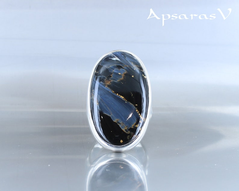 Puede incluir: Un anillo de plata con una gran piedra ovalada azul y negra con motas doradas. La piedra tiene un patr&oacute;n de remolino.