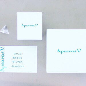 Peut inclure: Trois bo&icirc;tes blanches avec le texte "Apsaras V" en lettres bleu turquoise. La plus petite bo&icirc;te porte le texte "Gold Stone Silver Jewelry" en lettres bleu turquoise.