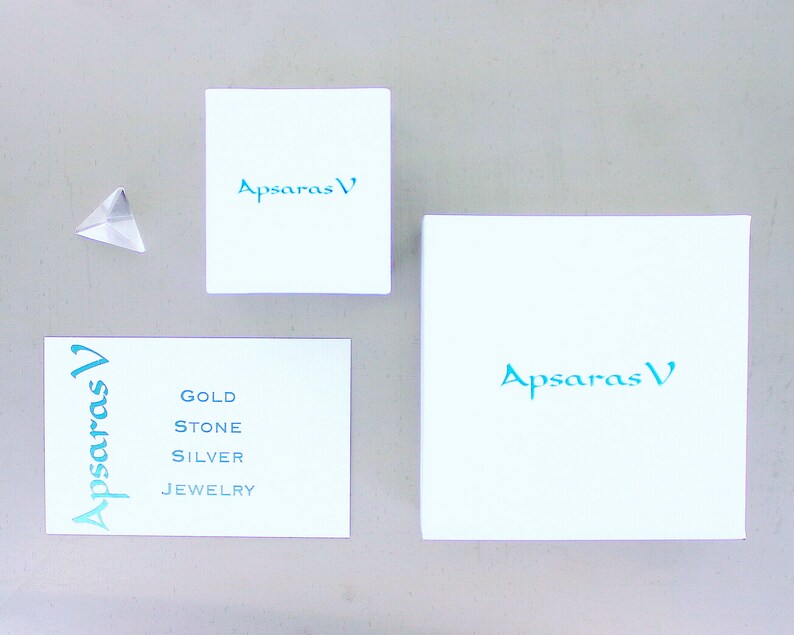 Peut inclure: Trois bo&icirc;tes blanches avec le texte "Apsaras V" en lettres bleu turquoise. La plus petite bo&icirc;te porte le texte "Gold Stone Silver Jewelry" en lettres bleu turquoise.