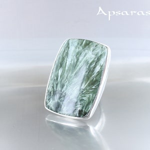 May include: A silver ring with a large, rectangular green gemstone. The gemstone has a swirling, cloudy pattern.