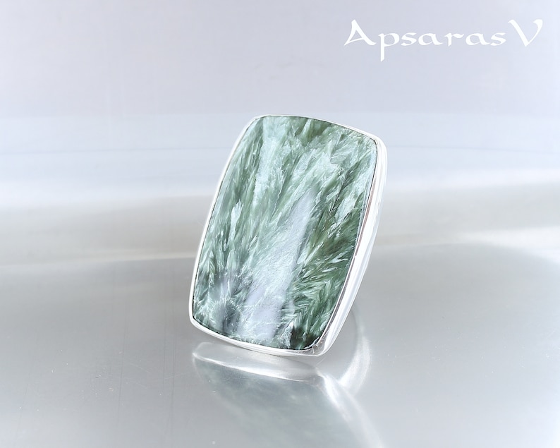 May include: A silver ring with a large, rectangular green gemstone. The gemstone has a swirling, cloudy pattern.