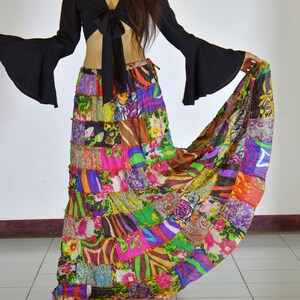 Puede incluir: Una falda larga de patchwork colorida con un top corto negro con un lazo en la parte delantera. La falda está hecha de varias telas y patrones, incluyendo estampados florales, rayas y paisley.