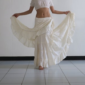 Puede incluir: Un top blanco de hombros descubiertos con una falda con volantes. La falda es de capas y tiene un diseño fluido.