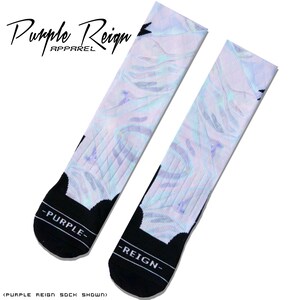 Pode incluir: Um par de meias brancas com um padrão holográfico iridescente. As meias têm uma borda preta e as palavras "Purple Reign" e "Purple" são impressas nas meias.