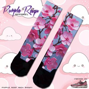 Könnte beinhalten: Ein Paar Socken mit einem floralen Design mit rosa Kirschblüten auf hellblauem Hintergrund. Die Socken sind oben und unten schwarz. Der Text "Purple Reign Apparel" befindet sich oben im Bild. Der Text "(Purple Reign Sock Shown)" befindet sich unten im Bild. Der Text "Inspired By:" befindet sich unten rechts im Bild. Ein rosa-weißer Laufschuh ist unter dem Text abgebildet.