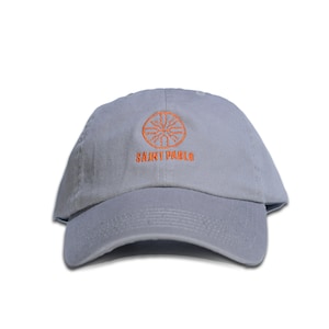 Könnte beinhalten: Eine graue Baseballkappe mit einem orangefarbenen gestickten Logo. Das Logo ist ein Kreis mit einem Sternenausbruch-Design und dem Text "SAINT PABLO" darunter.