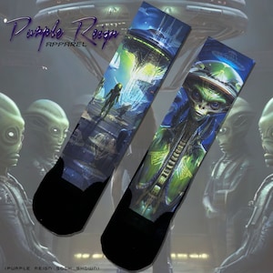 May include: A pair of black socks with a colorful graphic print of an alien and a spaceship. The socks feature a blue, green, and yellow color scheme. The text "Purple Reign Apparel" is visible in the top left corner of the image.