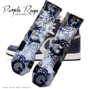 Puede incluir: Un par de calcetines deportivos azules y blancos con estampado de galaxia y un gráfico de bulldog. Los calcetines se muestran con un par de zapatillas de deporte azul marino y blancas. El texto "Purple Reign Apparel" es visible en la esquina superior izquierda de la imagen. El texto "Nike Elite Sock Shown" es visible en la esquina inferior izquierda de la imagen.