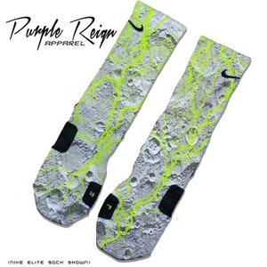 May include: A pair of white and grey socks with a neon green moon-like pattern and a black Nike swoosh logo. The socks are Nike Elite socks.