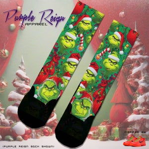 May include: A pair of black and green Christmas themed socks with a repeating pattern of the Grinch wearing a Santa hat. The socks are on a background of a Christmas tree and presents.