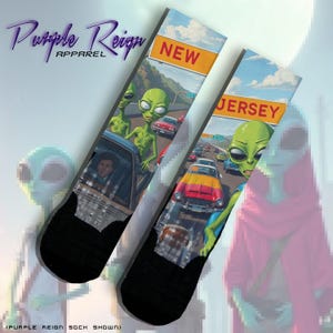 May include: A pair of black socks with a graphic print of aliens driving cars on a highway. The socks feature the text "New Jersey" and "Purple Reign Apparel".