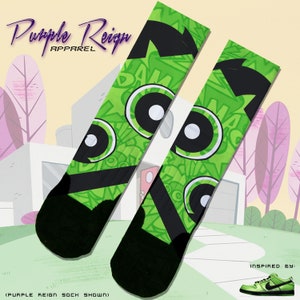 Può includere: Un paio di calzini verdi e neri con un occhio di cartone animato e una stampa grafica "BAM". I calzini sono ispirati al personaggio dei cartoni animati Dexter's Laboratory. Il testo "Purple Reign Apparel" è visibile nella parte superiore dell'immagine.