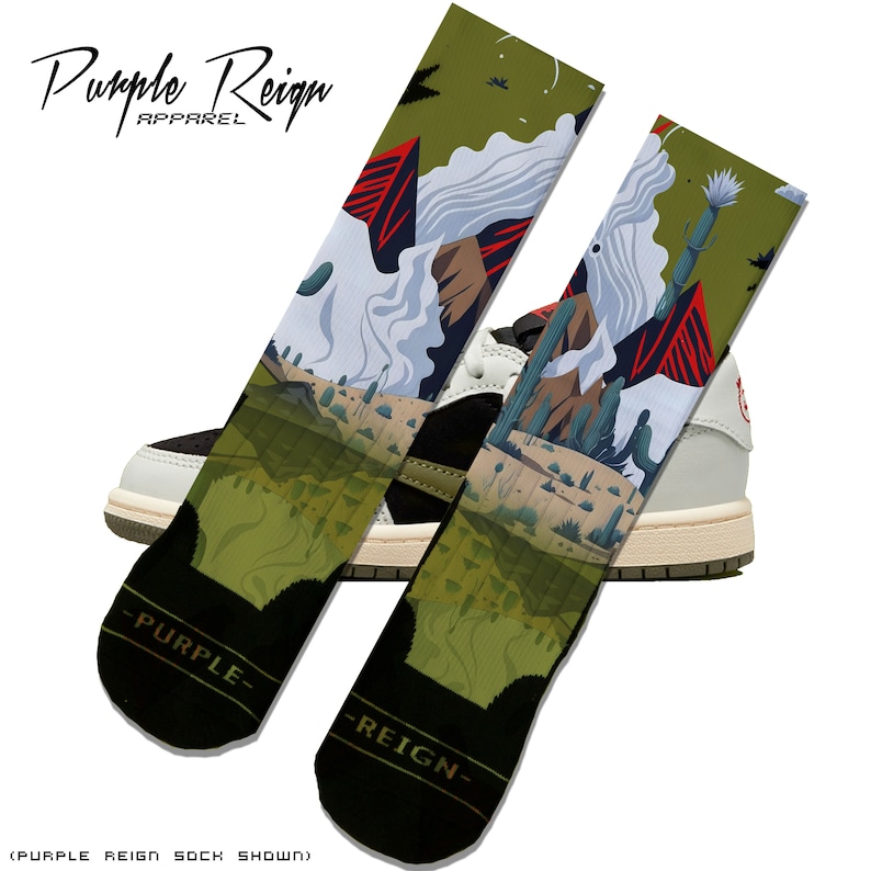 May include: Two socks with a desert landscape design, featuring mountains, cacti, and a cloudy sky. The socks are olive green and black, with the text "Purple Reign" at the top and bottom. The socks are displayed in front of a black and white sneaker.